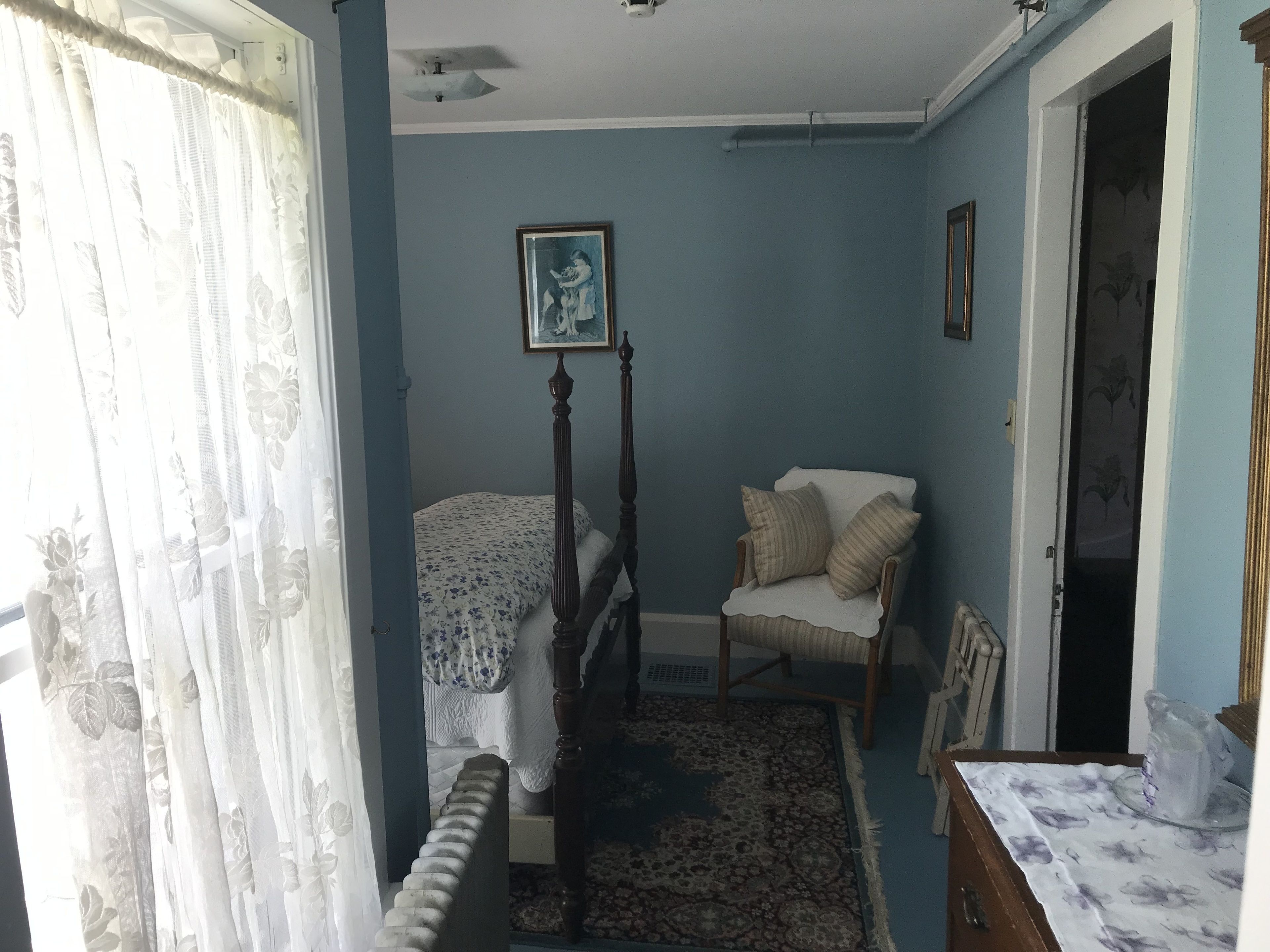 A bedroom with a bed, a chair, a radiator, and a picture on the wall.