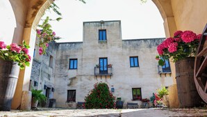 A courtyard with a building, stone pathway, and potted plants. - Agriturismo Baglio Fontana (Buseto Palizzolo)