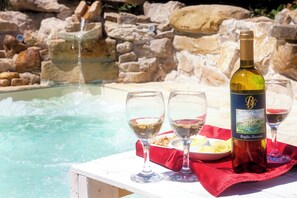 Escena junto a la piscina con una botella de vino, copas y un plato de aperitivos.