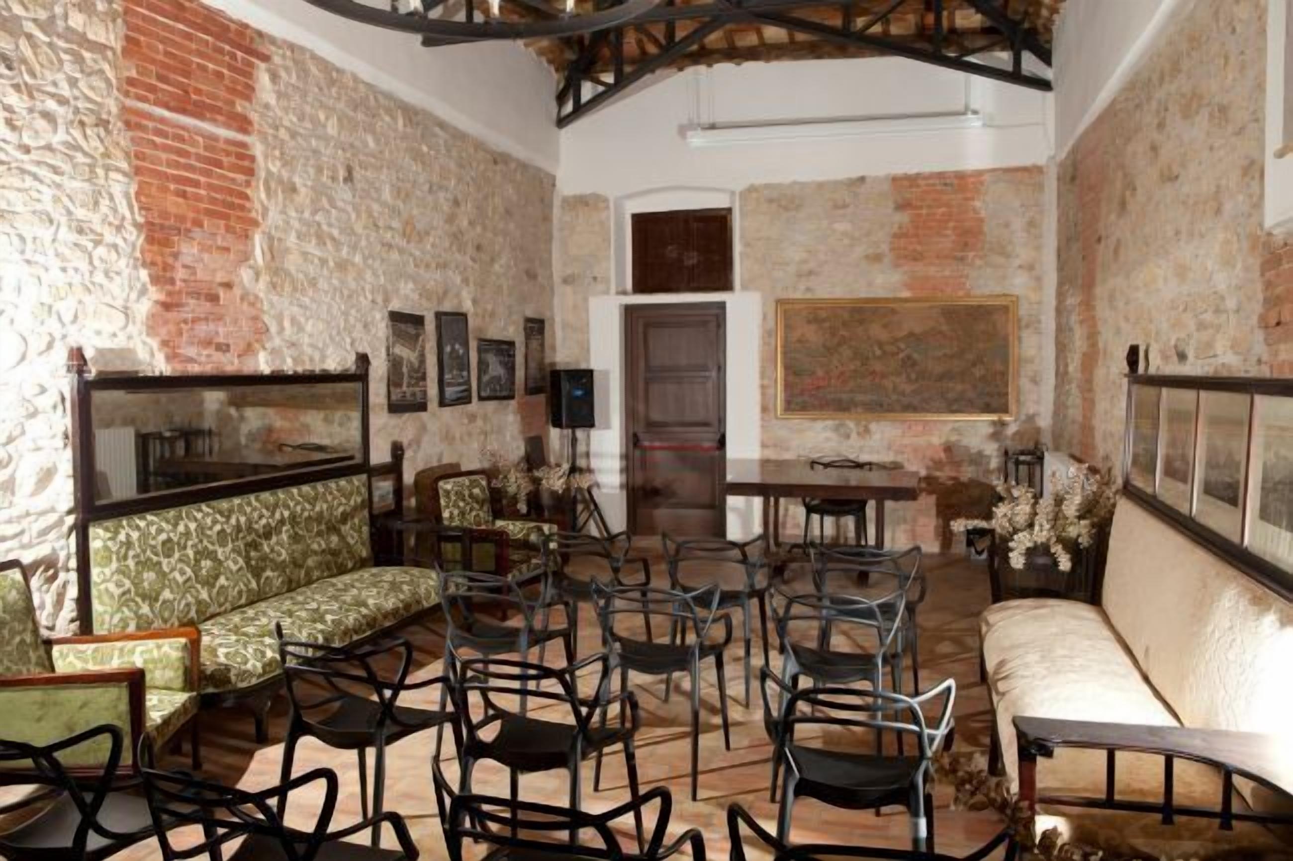 A rustic interior with stone walls, a wooden ceiling, and a mix of seating including a sofa, chairs, and a table.
