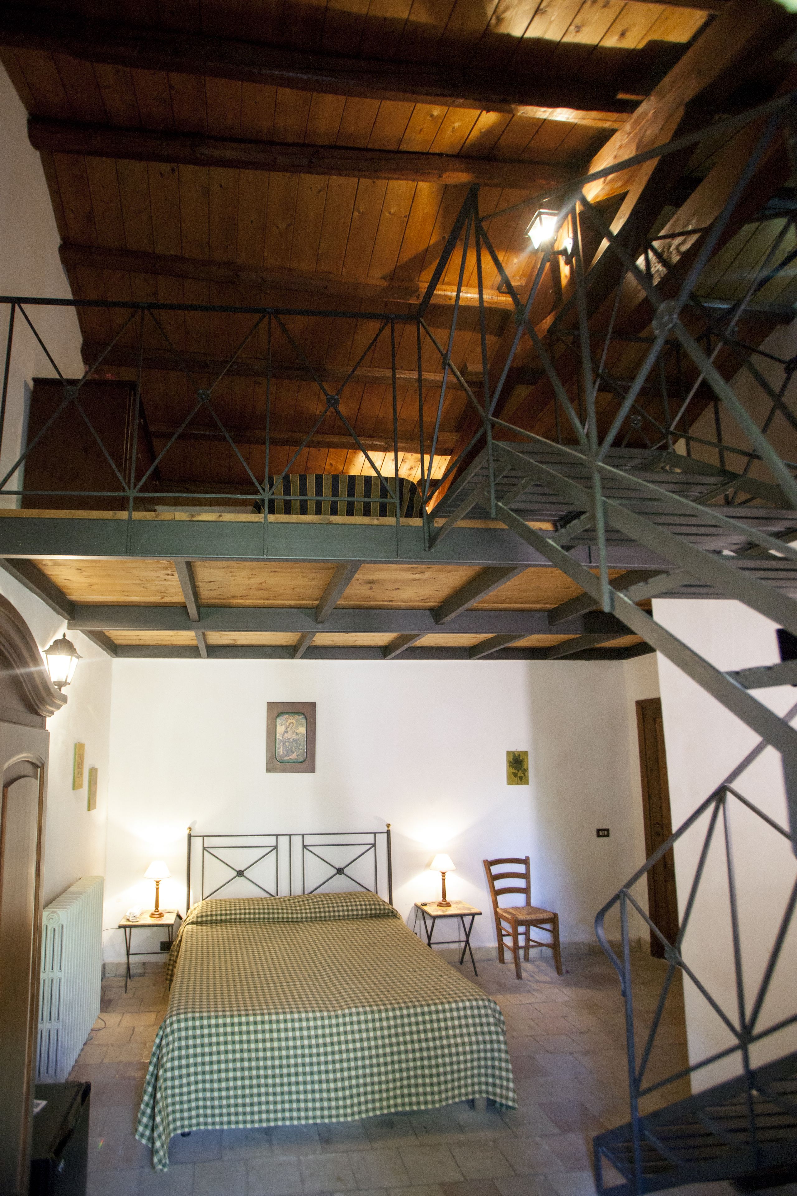 Una camera da letto con soffitto in legno, un letto con copripiumino a quadretti, una sedia e un tavolino con una lampada.