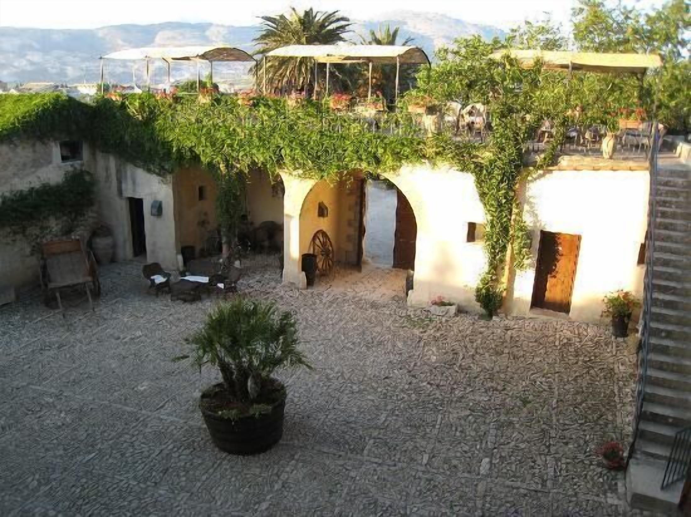 Une cour intérieure agrémentée d’arcades, de plantes en pot et d’un sol en pierre rustique.