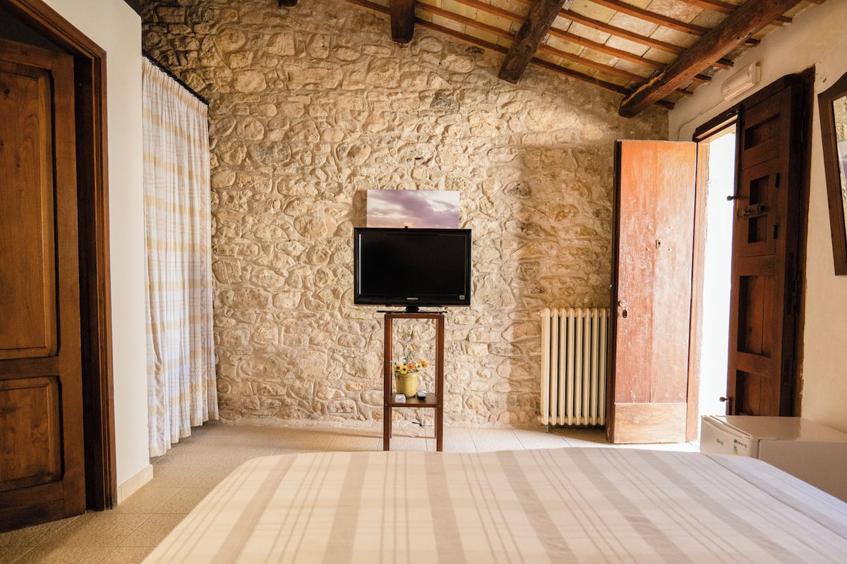 Een kamer met een stenen muur, een televisie op een houten standaard, een radiator en een houten deur.