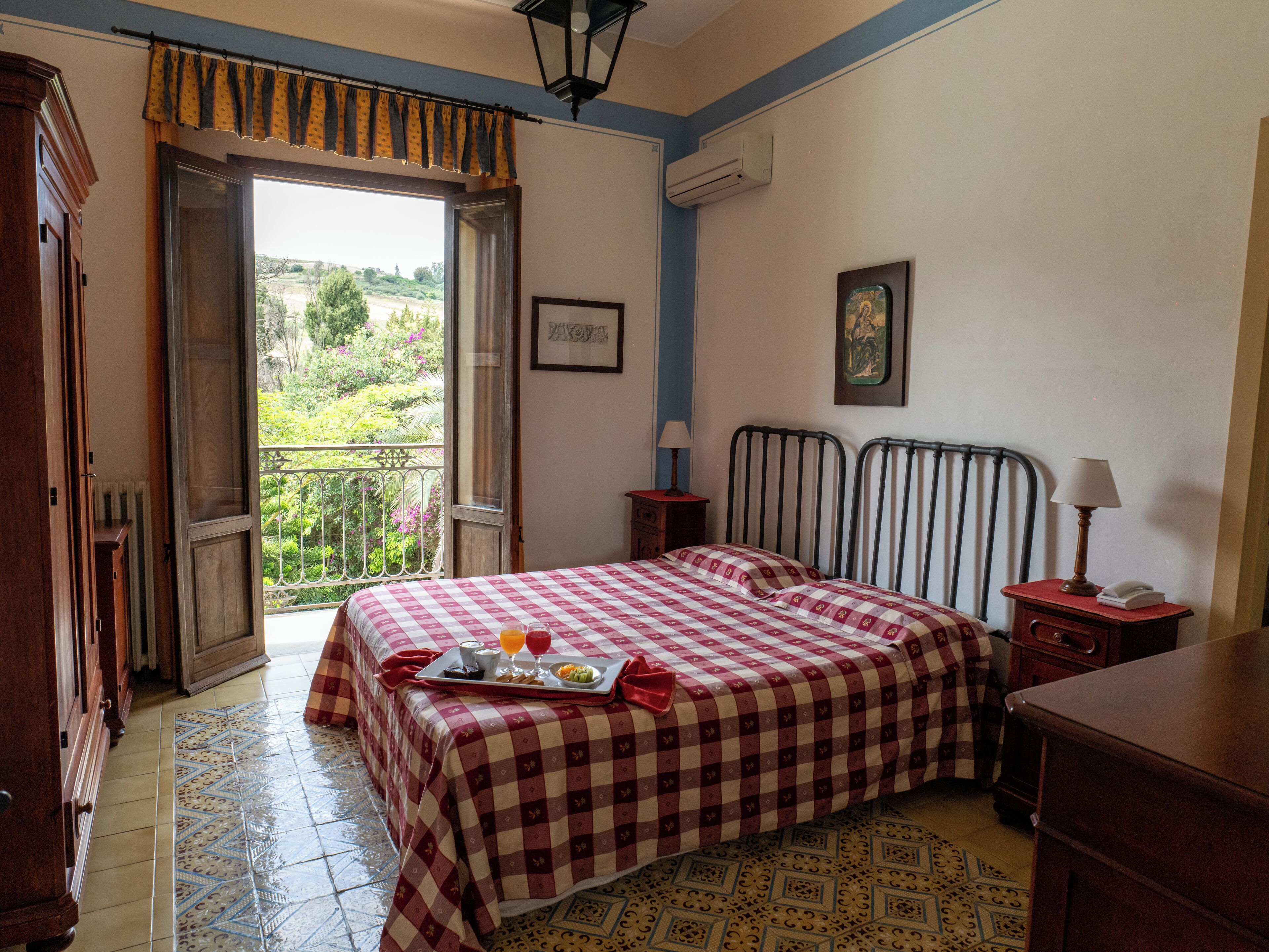 Un dormitorio con colcha a cuadros, una bandeja con desayuno y un balcón con vistas.