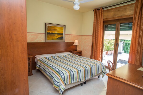 Una habitación de hotel con cama, mesita de noche, lámpara, un cuadro en la pared y vistas al exterior a través de una ventana.