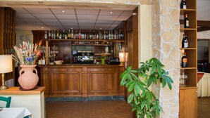 Een bar met een stenen muur, houten planken met flessen en een aanrecht met een koffieapparaat.