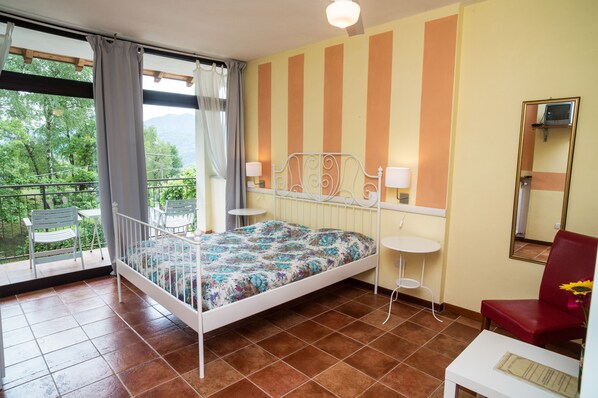 Un dormitorio con cama, una silla, una mesita, un espejo y un balcón con sillón y mesa.