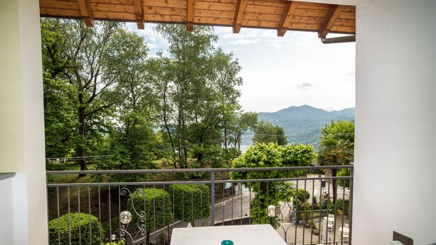 Een balkon met een witte tafel en stoelen, met uitzicht op een weelderige tuin en verre bergen.