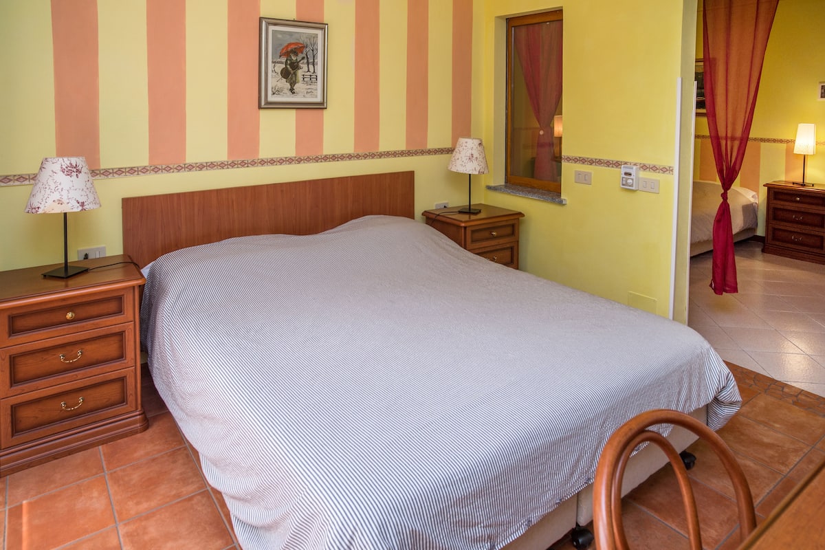 A hotel room with a bed, bedside tables, lamps, a wall clock, and a window with curtains.