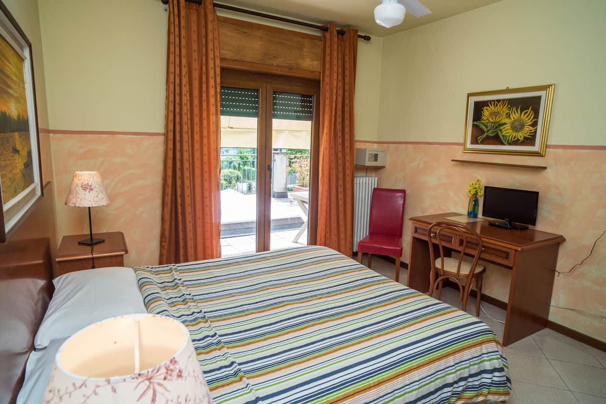 A hotel room with a bed, a desk with a chair, a television, and a window with curtains.