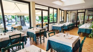 Een restaurant met meerdere tafels en stoelen, grote ramen en uitzicht op de omgeving.