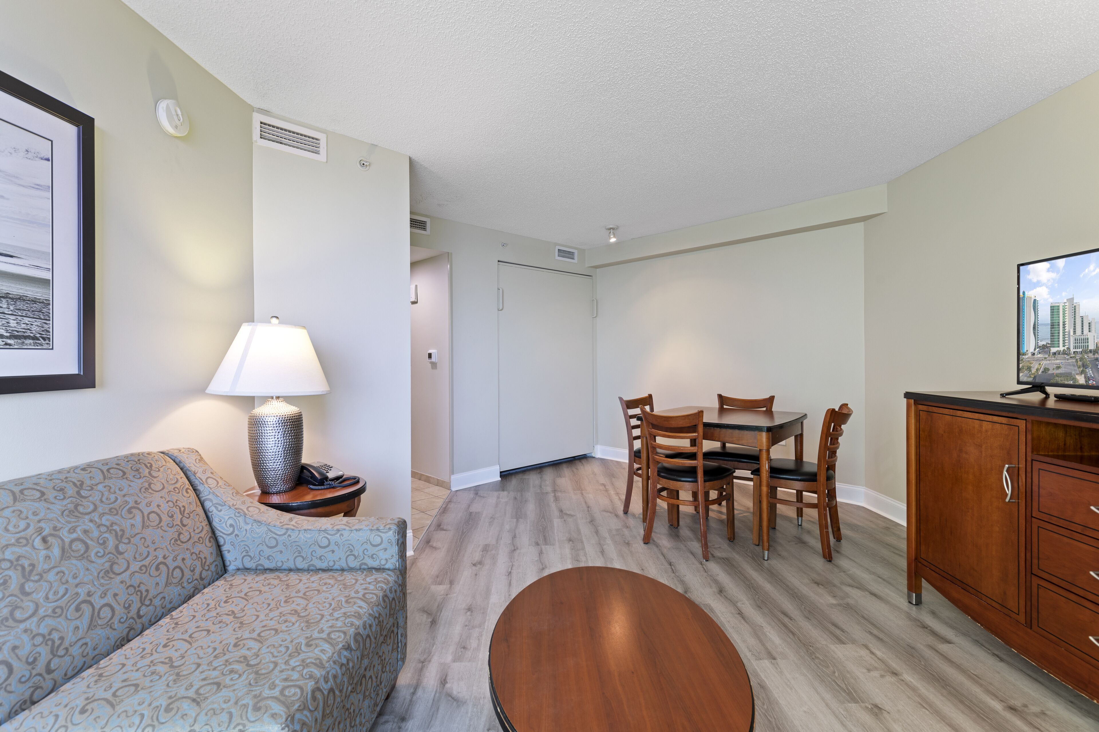 Une chambre d’hôtel avec un canapé à motifs, une table ronde, des chaises en bois, une télévision et un meuble.