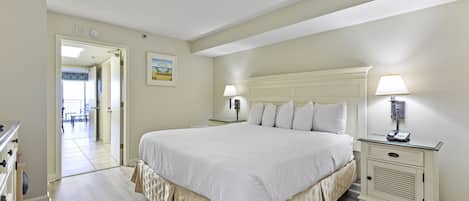 A bedroom with a large bed, bedside tables, a dresser, and a door leading to another room.