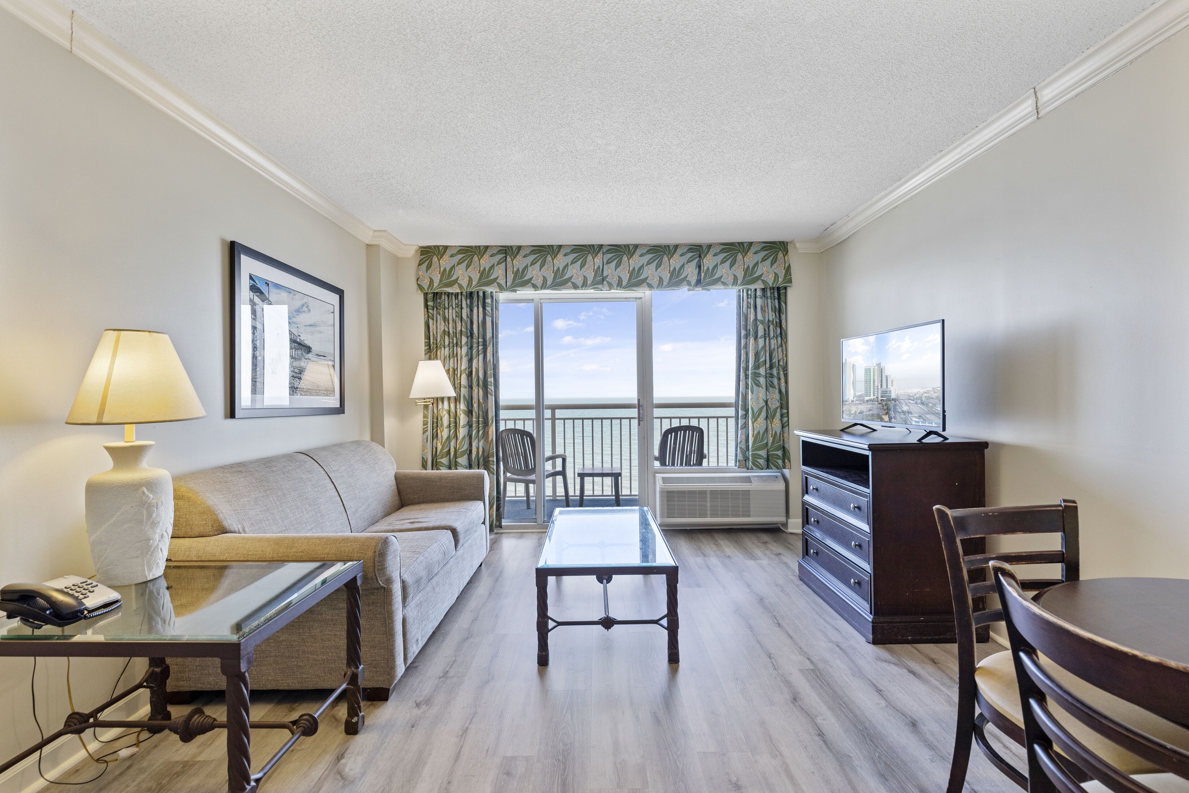 Une chambre d’hôtel avec un canapé, une table à plateau en verre, une chaise, un téléviseur et un balcon avec vue.