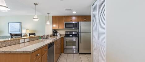 A modern kitchen with wooden cabinets, stainless steel appliances, and a tiled floor.