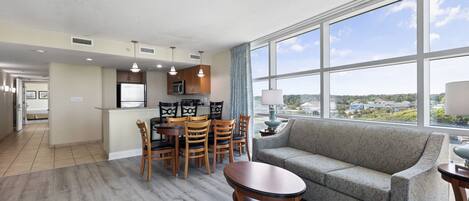A modern hotel room with a dining area, a sofa, and large windows offering a city view.