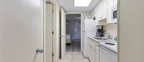 A narrow kitchen with white cabinets, a refrigerator, a microwave, and a coffee maker.