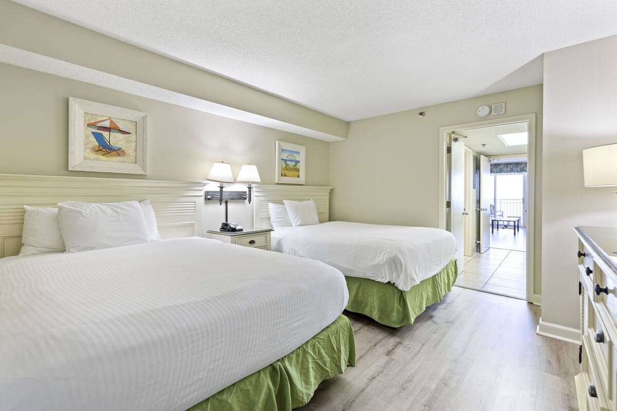 Habitación de hotel con dos camas, una mesita de noche con lámparas, un cuadro y vistas al exterior.