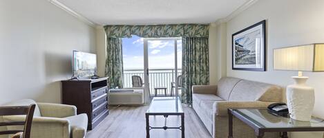 A hotel room with a balcony, a sofa, a chair, a coffee table, and a TV.