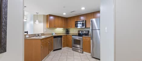 A modern kitchen with wooden cabinets, stainless steel appliances, and a tiled floor.