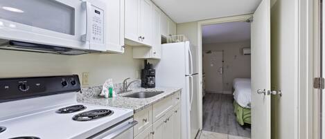 A compact kitchen with a microwave, stove, sink, and refrigerator.