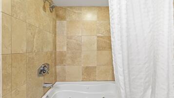 A bathroom with beige tiles, a white bathtub, and a showerhead.