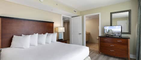 Une chambre d’hôtel avec un grand lit, une commode avec un téléviseur et une porte donnant sur une autre pièce.