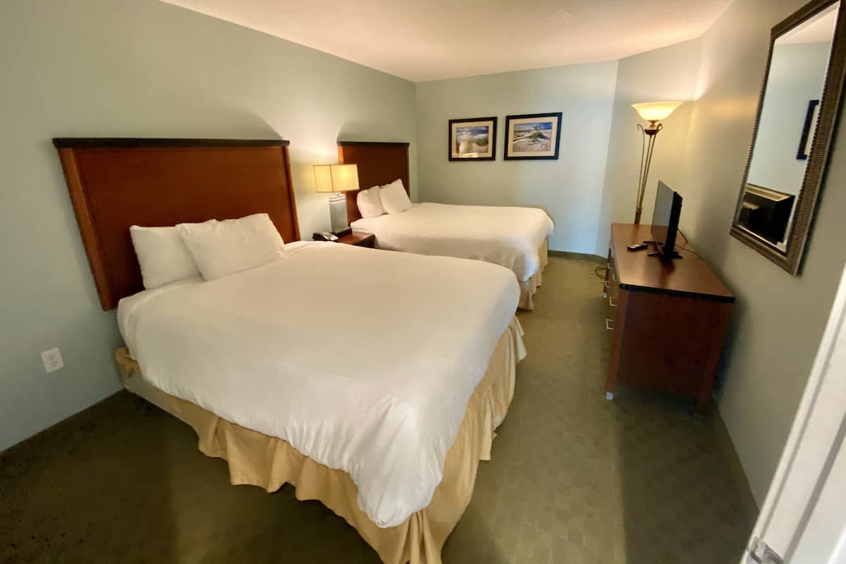 Una habitación de hotel con dos camas, una mesita de noche con lámpara, un aparador y un espejo.