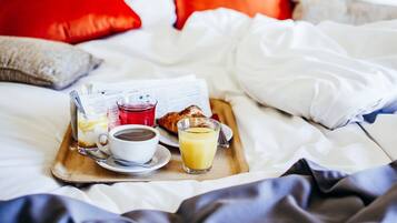 Un safata de matí sobre un llit amb un diari, una tassa de cafè, un got de suc d'aranja i un croissant.