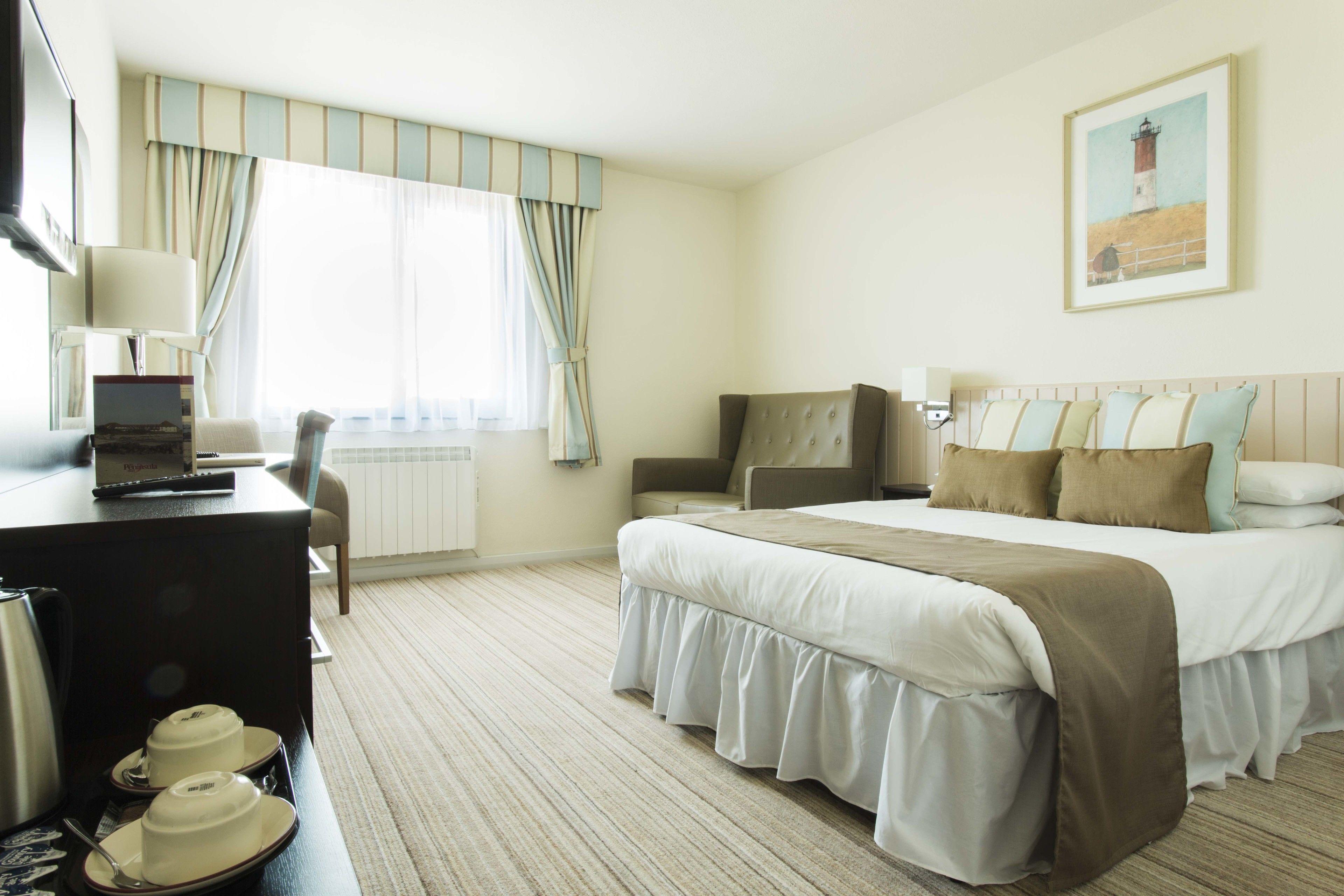 Ein Hotelzimmer mit einem Bett, einem Schreibtisch mit einem Laptop, einem Sessel und einem Esstisch.