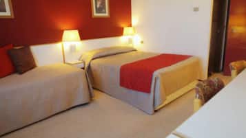 Quarto de hotel com duas camas, cada uma com um cobertor vermelho e luminárias laterais.