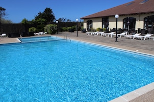 Una piscina con sillones de descanso y un edificio con techo de tejas al fondo.