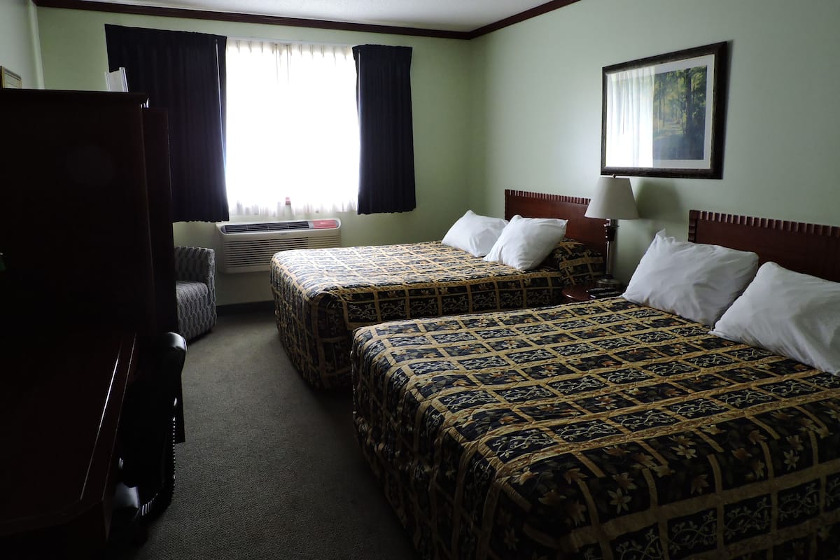 A hotel room with two beds, a desk, a chair, a TV, and a window with curtains.