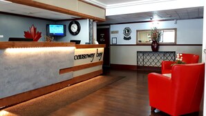 Un área de recepción con un mostrador de madera, un reloj, un televisor y una silla roja.