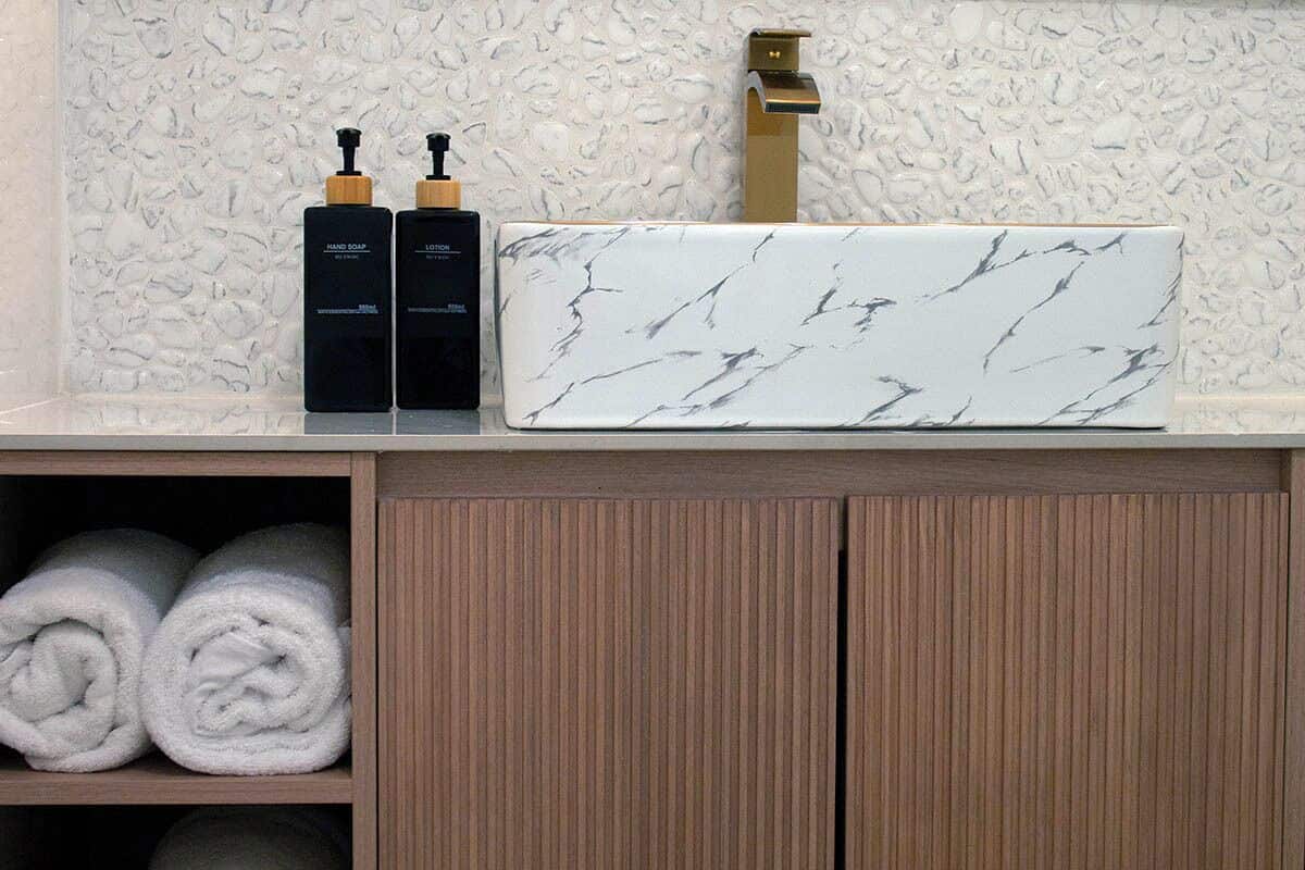 A bathroom with a marble-patterned sink, two hand soap bottles, and neatly rolled towels on shelves.