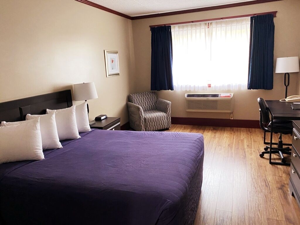 A hotel room with a large bed, a chair, a desk, and a window with curtains.