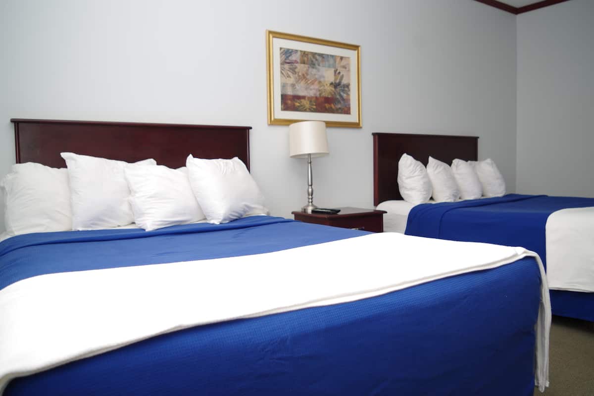 A hotel room with two beds, each with white and blue bedding, a nightstand with a lamp, and a painting on the wall.