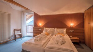 A double bed with towels, a wooden chair, a nightstand, and a wooden wardrobe in a room with a wooden ceiling and a view through a window. - Hotel Alle Piramidi (Segonzano)