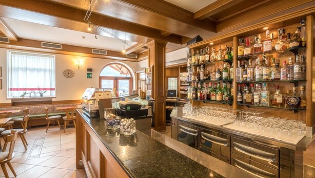 A bar area with a variety of liquor bottles, a cash register, and a seating area with tables and chairs. - Hotel Alle Piramidi (Segonzano)