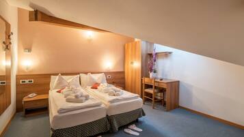 Una habitación de hotel con cama, mesita de noche, lámpara, escritorio, silla y pantuflas.