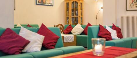 A room with green sofas, red and white cushions, a wooden cabinet, and a framed picture on the wall.