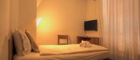 Una habitación de hotel con una cama, televisión montada en la pared, una silla y una mesita de noche.