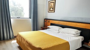 A neatly made bed with a yellow bedspread and white pillows, a wooden nightstand with a lamp, and a window with curtains. - Art & Hotel Treviolo (Treviolo)
