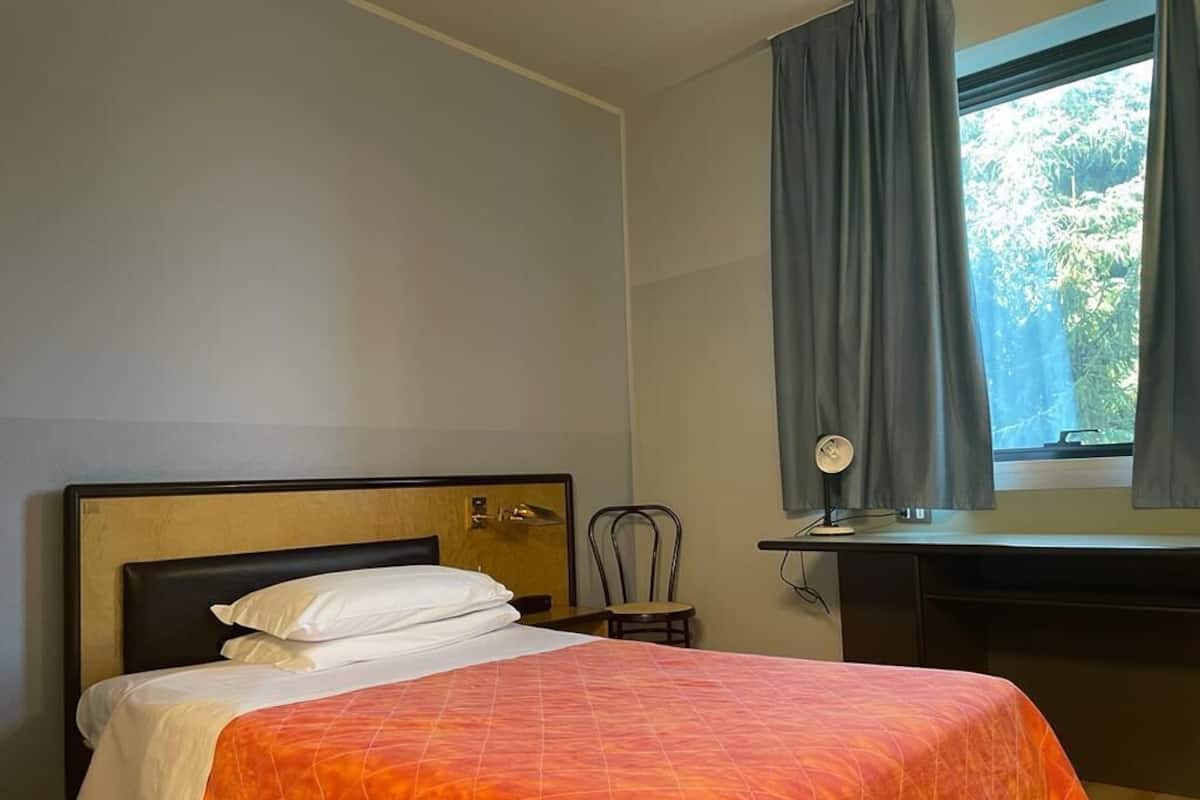 Ein Hotelzimmer mit einem Bett, einem Schreibtisch und einem Fenster mit Vorhängen.