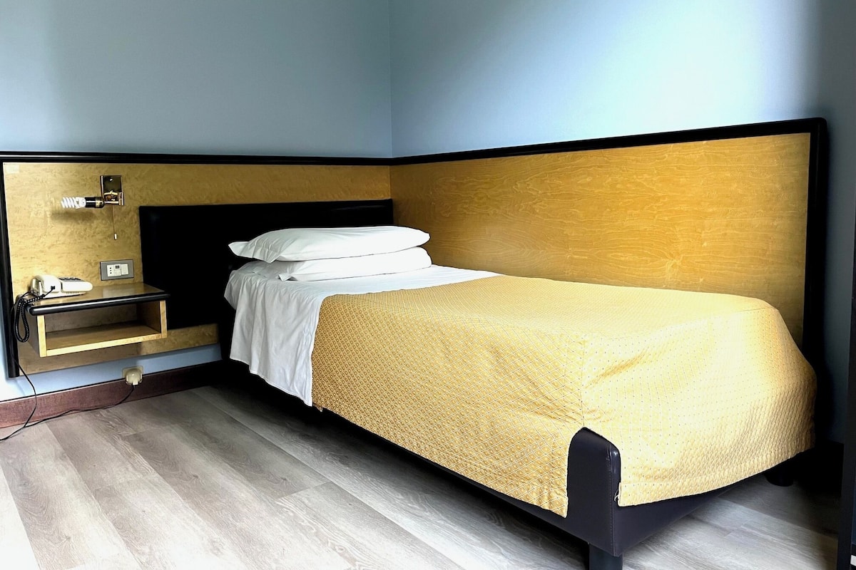 Ein Einzelbett mit Holz-Kopfteil, ein Nachttisch mit Lampe und ein Telefon.