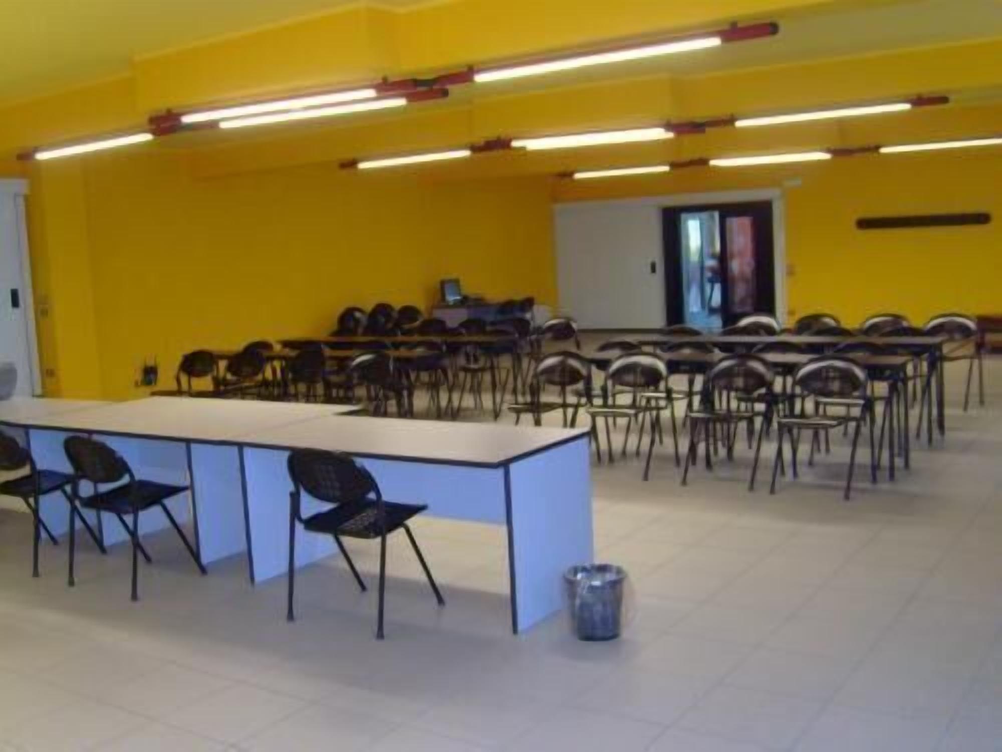 A conference room with a long table and chairs, fluorescent lighting, and a tiled floor.