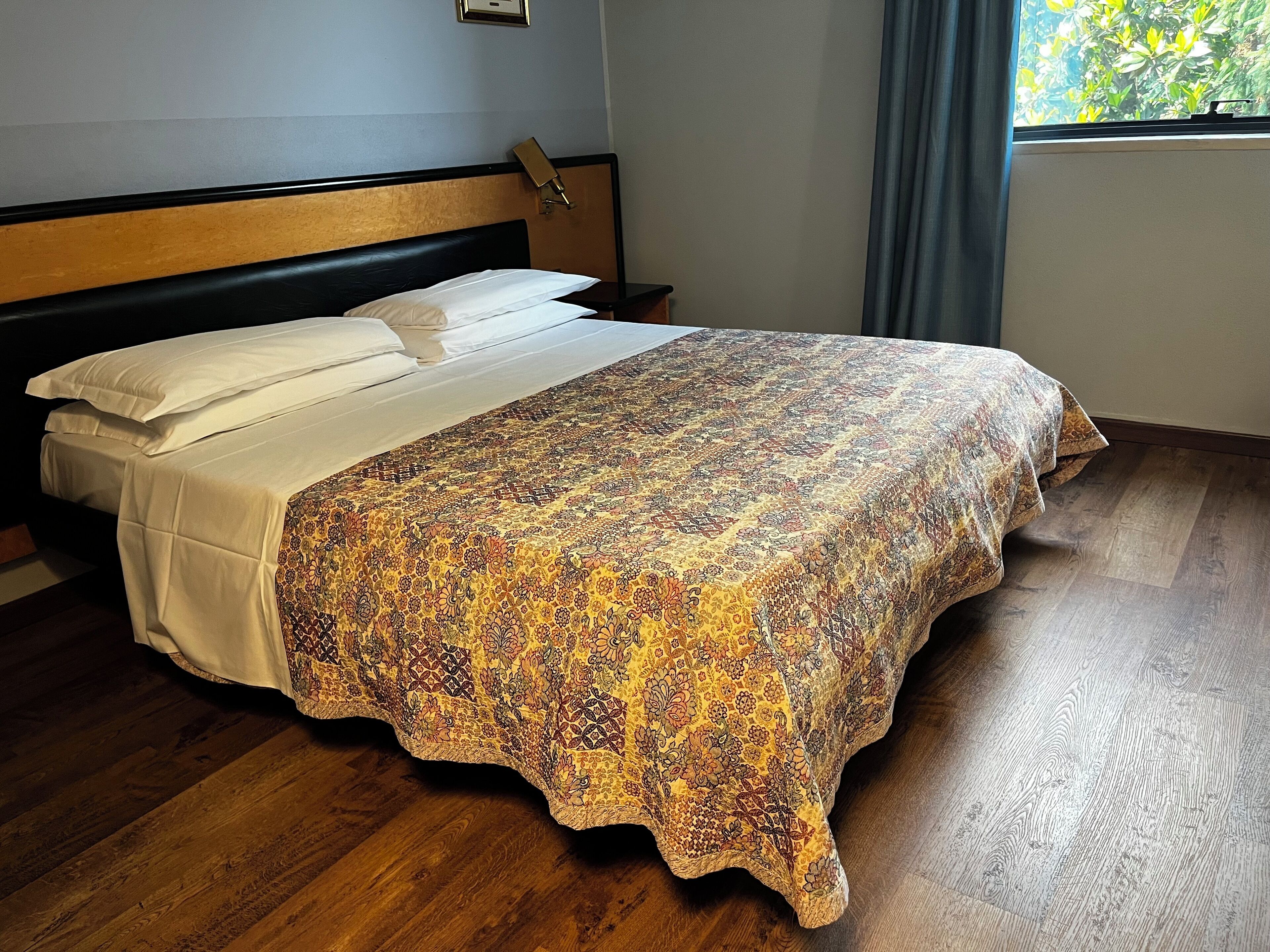 Ein ordentlich bezogenes Bett mit einem gemusterten Überwurf und weißen Leinentüchern, einem Holz-Kopfteil und einem Nachttisch mit einer Lampe.