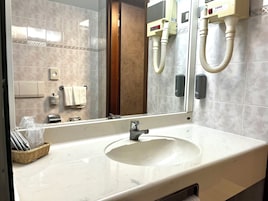 Un bagno d'albergo con lavandino, specchio, dispenser di asciugamani e asciugacapelli a parete.