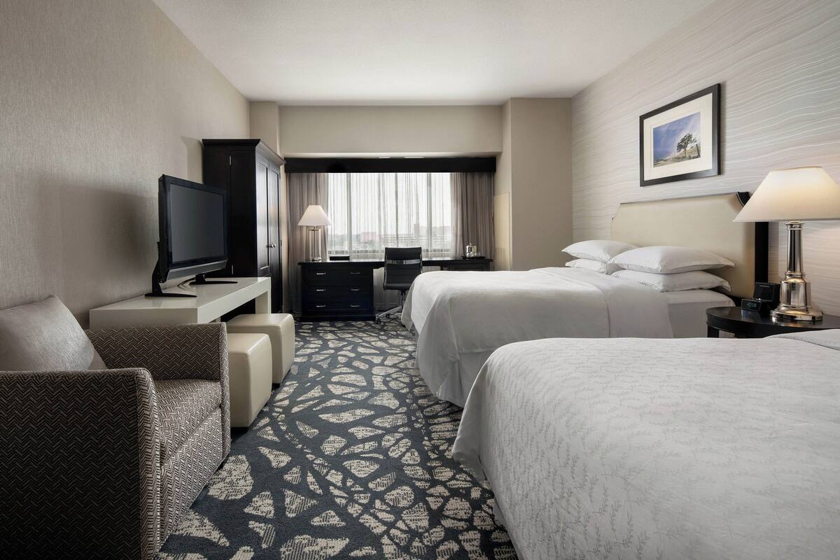 Ein Hotelzimmer mit Fernseher, zwei Betten, einem Schreibtisch und einem Sessel.