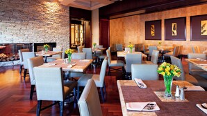A spacious restaurant with high ceilings, stone walls, and a fireplace. Tables are set with chairs, and there are framed artworks on the walls. - Sheraton Garden Grove-Anaheim South Hotel (Garden Grove)